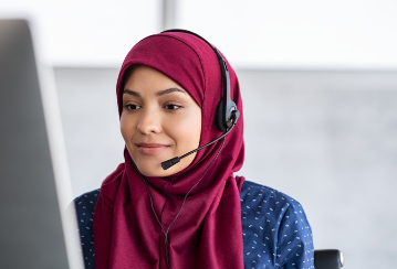 A woman wearing a headset smiles as she works at her computer.